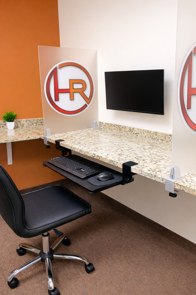 Ergonomic testing workstation at EverythingHR Talent Development Institute with wall-mounted monitor, adjustable keyboard tray, and privacy dividers